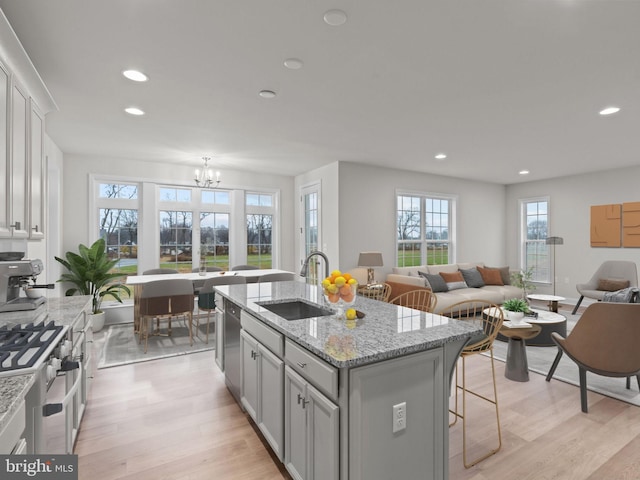 kitchen with an island with sink, sink, light hardwood / wood-style floors, stainless steel appliances, and light stone countertops