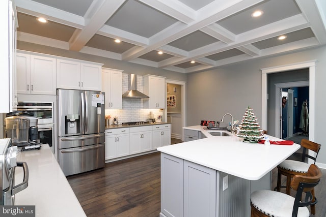 kitchen featuring white cabinetry, wall chimney range hood, stainless steel appliances, and a kitchen island with sink