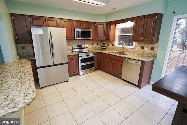 kitchen featuring stainless steel appliances, light stone counters, tasteful backsplash, and sink