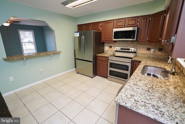 kitchen with sink, decorative backsplash, ceiling fan, light stone countertops, and appliances with stainless steel finishes