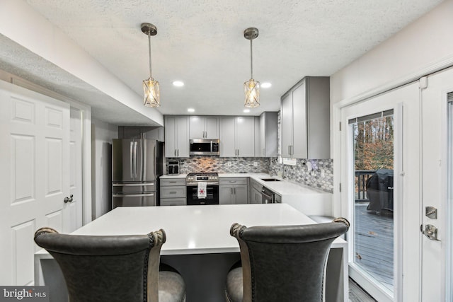 kitchen with backsplash, gray cabinetry, stainless steel appliances, hanging light fixtures, and a breakfast bar area