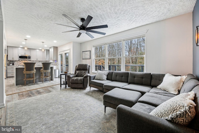 living room with ceiling fan, a textured ceiling, and light wood-type flooring