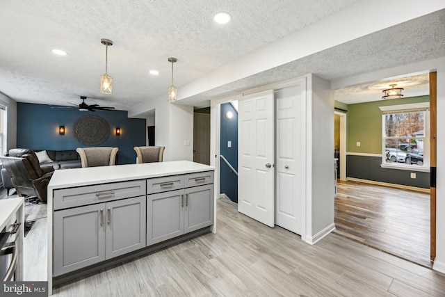 kitchen with decorative light fixtures, gray cabinets, a textured ceiling, and light hardwood / wood-style flooring