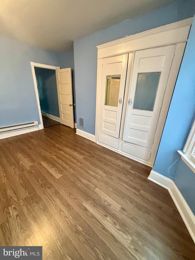 unfurnished bedroom featuring a baseboard heating unit, wood-type flooring, and a closet