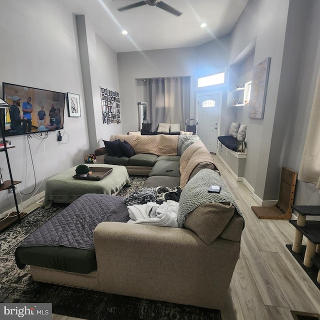 living room with ceiling fan, a high ceiling, and light wood-type flooring