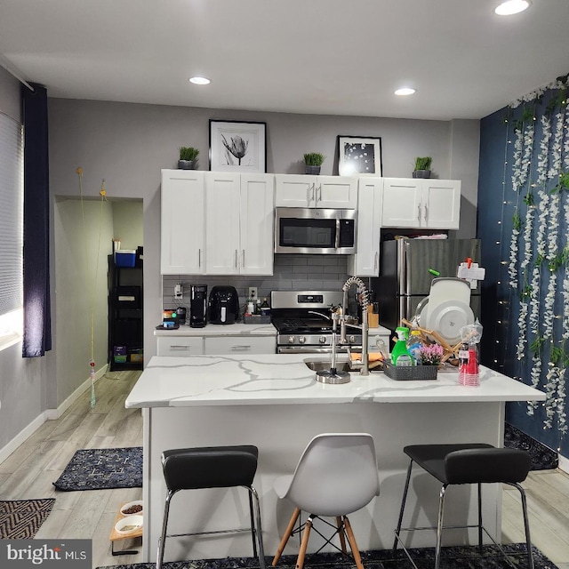 kitchen featuring a kitchen island with sink, light hardwood / wood-style flooring, appliances with stainless steel finishes, white cabinetry, and a breakfast bar area