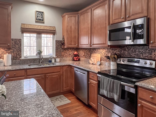 kitchen featuring stone countertops, sink, stainless steel appliances, and light hardwood / wood-style flooring