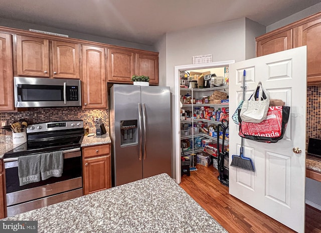 kitchen with light stone countertops, hardwood / wood-style floors, backsplash, and stainless steel appliances