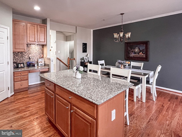 kitchen with light stone countertops, wood-type flooring, decorative light fixtures, a chandelier, and a center island