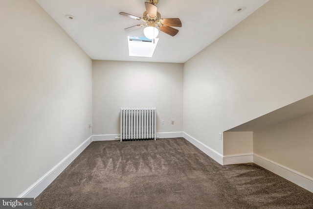 spare room with ceiling fan, a skylight, radiator, and dark colored carpet