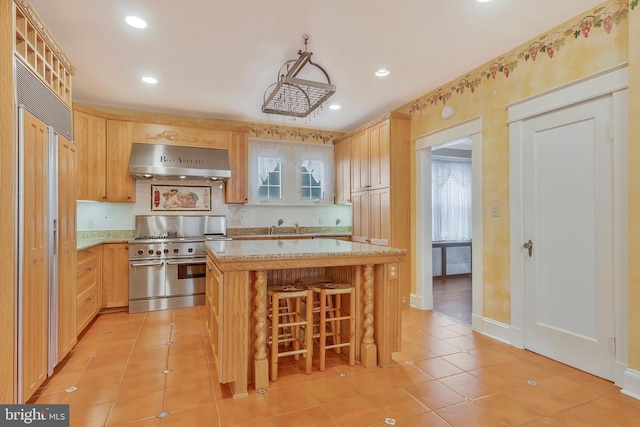 kitchen featuring a kitchen island, a kitchen breakfast bar, exhaust hood, stainless steel range, and light brown cabinets