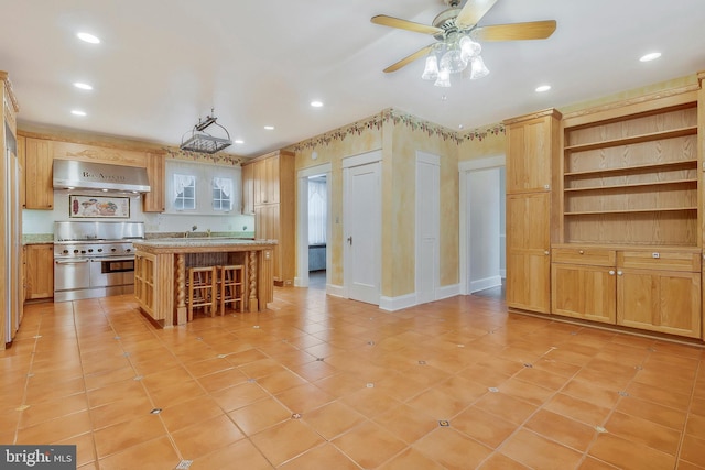 kitchen with a kitchen breakfast bar, a kitchen island, high end stainless steel range oven, ceiling fan, and exhaust hood