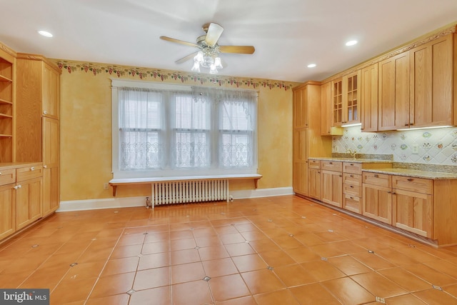 kitchen featuring ceiling fan, radiator, light tile patterned floors, and light stone counters