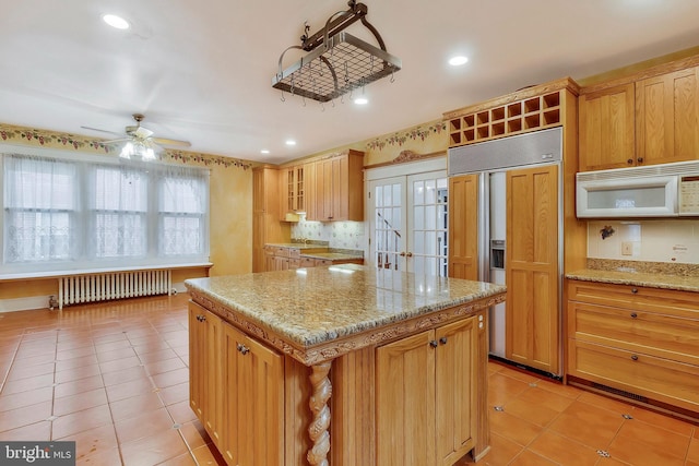 kitchen with a center island, light tile patterned floors, radiator heating unit, paneled built in fridge, and light stone countertops