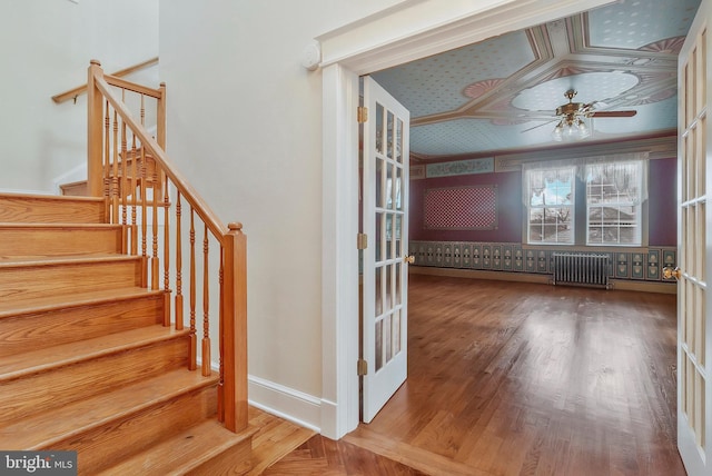 stairs with hardwood / wood-style floors, radiator heating unit, and ceiling fan