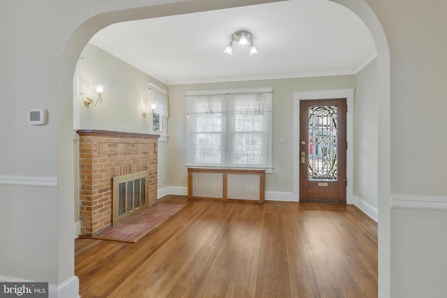 foyer entrance with a brick fireplace, crown molding, and wood-type flooring