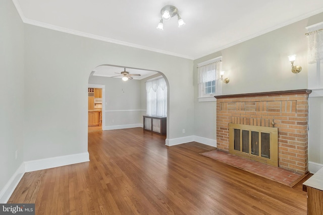 unfurnished living room with hardwood / wood-style flooring, crown molding, a brick fireplace, and ceiling fan