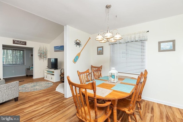 dining space featuring a chandelier, light wood-type flooring, and lofted ceiling