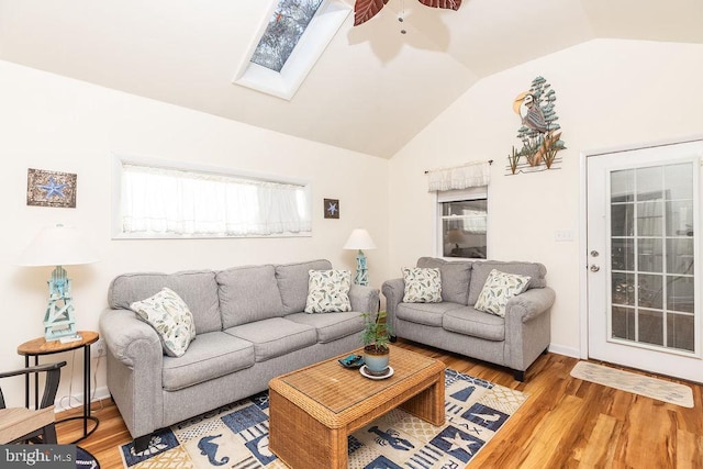 living room featuring hardwood / wood-style floors, ceiling fan, and vaulted ceiling with skylight