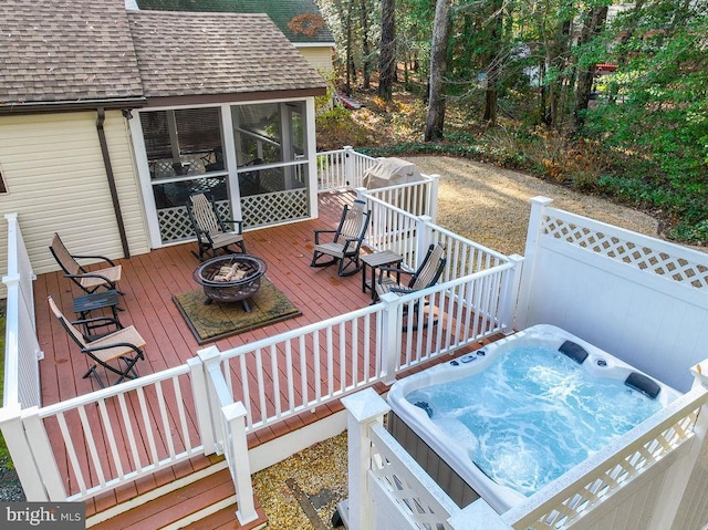 wooden deck with a fire pit, a hot tub, and a sunroom