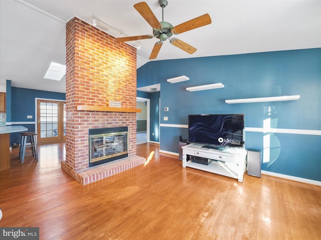 living room with ceiling fan, vaulted ceiling, a fireplace, and wood-type flooring