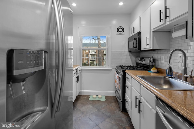 kitchen with backsplash, dark tile patterned flooring, sink, white cabinetry, and stainless steel appliances