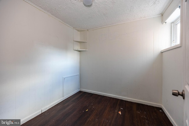 empty room featuring a textured ceiling, wooden walls, and dark wood-type flooring