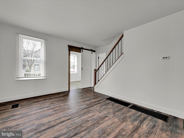 spare room featuring a barn door, plenty of natural light, and dark wood-type flooring