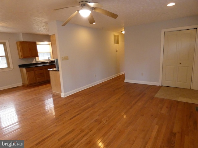 unfurnished living room featuring ceiling fan, sink, light hardwood / wood-style floors, and a textured ceiling