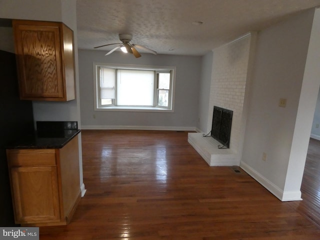 unfurnished living room with a textured ceiling, ceiling fan, dark wood-type flooring, and a brick fireplace