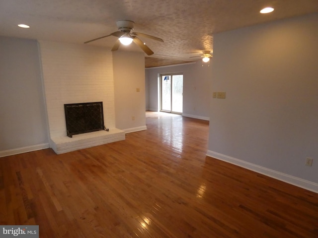 unfurnished living room with ceiling fan, a fireplace, wood-type flooring, and a textured ceiling