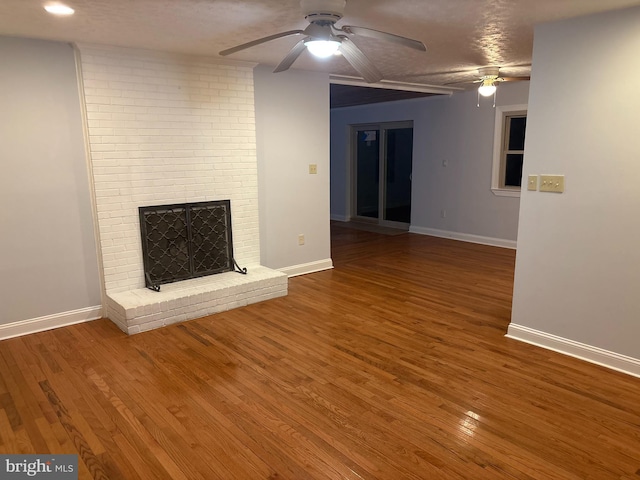 unfurnished living room with hardwood / wood-style floors, ceiling fan, a textured ceiling, and a brick fireplace