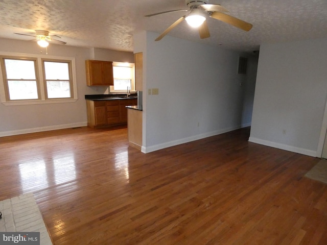 unfurnished living room with ceiling fan, sink, dark wood-type flooring, and a textured ceiling