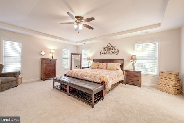 bedroom with multiple windows, light carpet, ceiling fan, and a tray ceiling