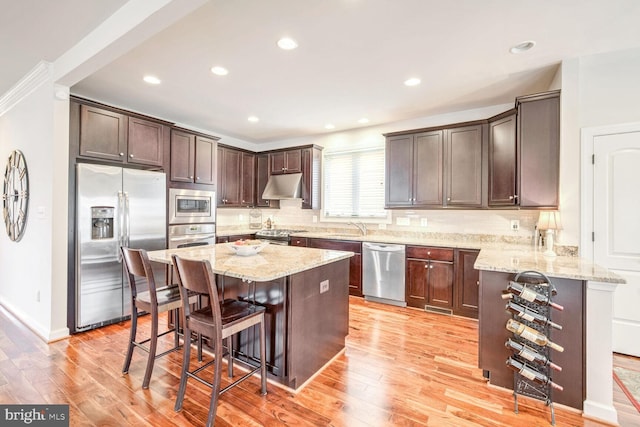 kitchen with sink, a breakfast bar area, stainless steel appliances, light stone countertops, and a kitchen island