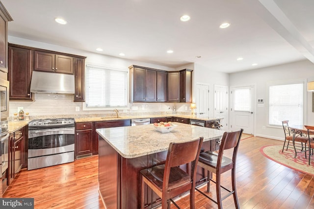 kitchen featuring light hardwood / wood-style flooring, a breakfast bar area, appliances with stainless steel finishes, light stone countertops, and a kitchen island