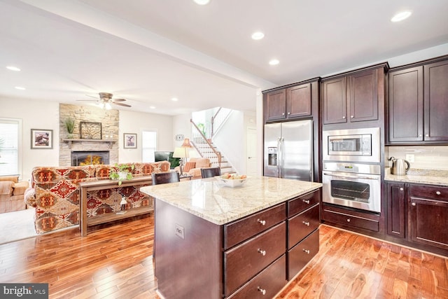 kitchen featuring stainless steel appliances, light stone countertops, dark brown cabinetry, and light hardwood / wood-style floors