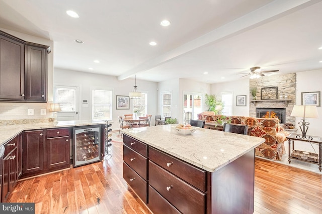 kitchen featuring a kitchen island, decorative light fixtures, beverage cooler, light hardwood / wood-style floors, and beam ceiling