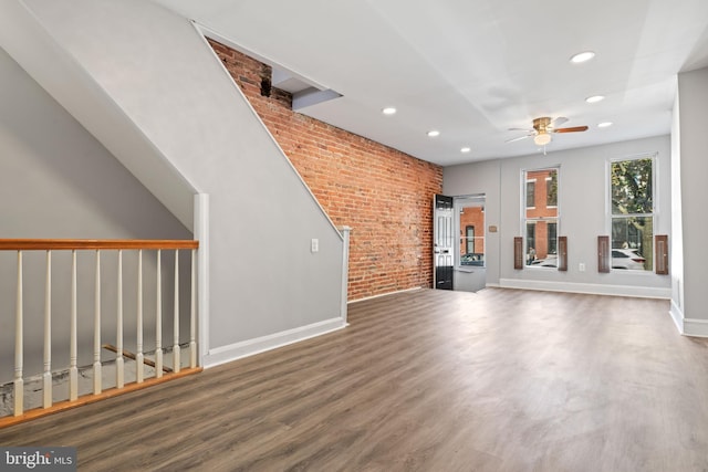 unfurnished living room with ceiling fan, brick wall, and dark hardwood / wood-style floors