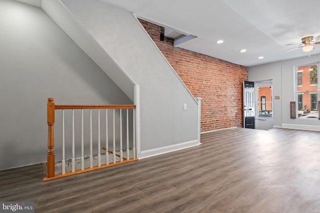 unfurnished living room with ceiling fan, dark wood-type flooring, and brick wall