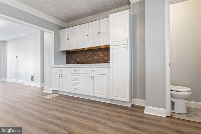 kitchen featuring white cabinets, ornamental molding, hardwood / wood-style floors, and a textured ceiling