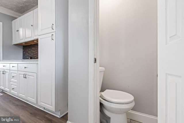 bathroom with wood-type flooring, backsplash, toilet, and crown molding