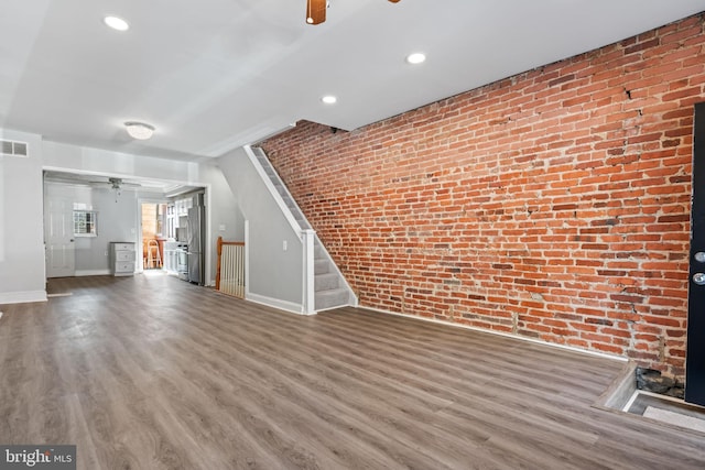 unfurnished living room with hardwood / wood-style floors and brick wall