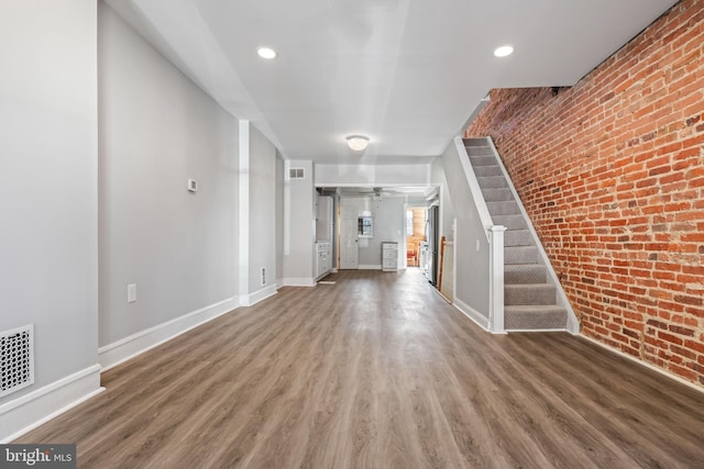 unfurnished living room with hardwood / wood-style floors, ceiling fan, and brick wall