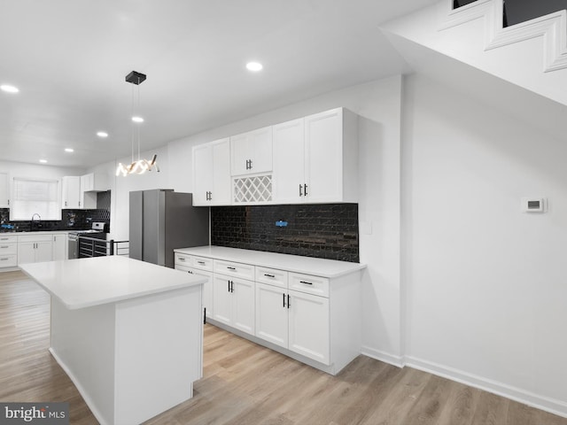 kitchen with white cabinets, light hardwood / wood-style floors, decorative light fixtures, a kitchen island, and appliances with stainless steel finishes