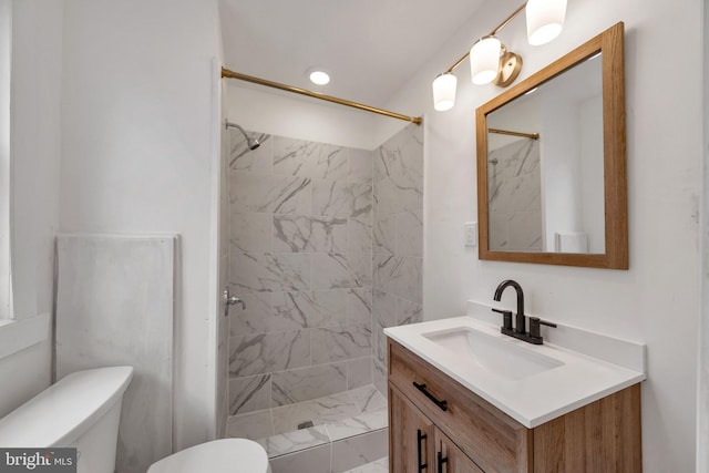 bathroom with a tile shower, vanity, and toilet