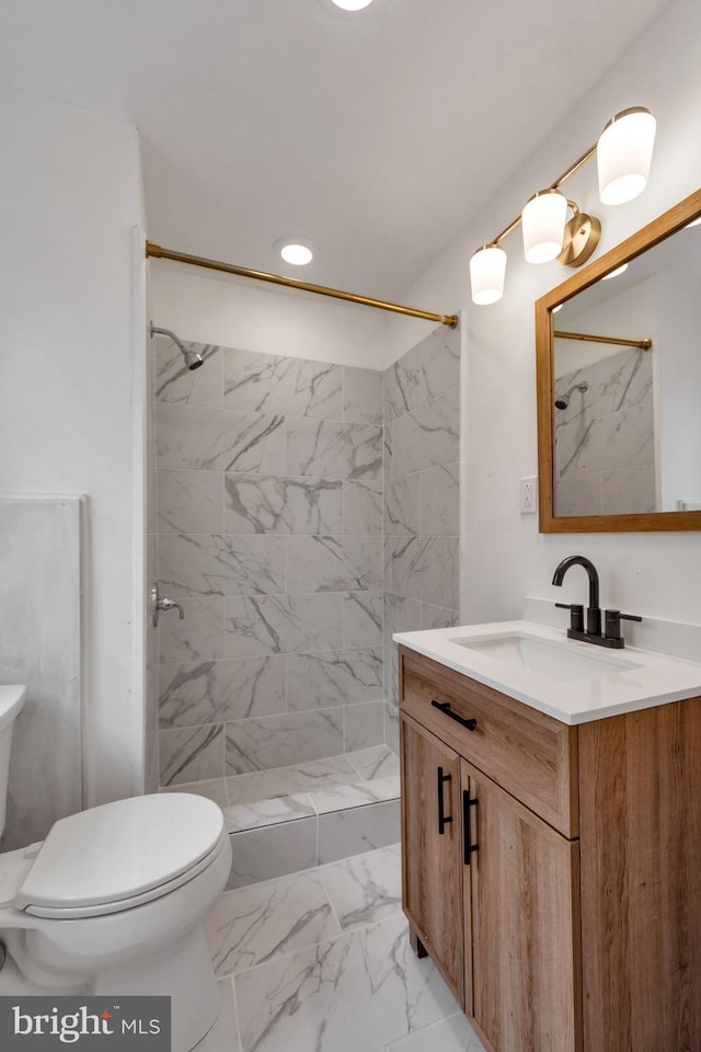 bathroom featuring a tile shower, vanity, and toilet