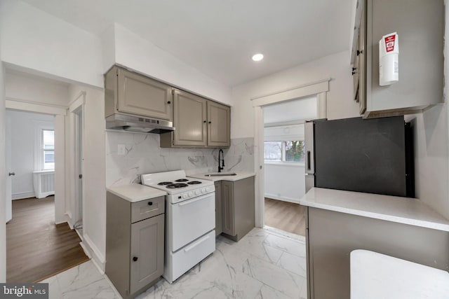 kitchen featuring tasteful backsplash, sink, exhaust hood, white stove, and stainless steel refrigerator