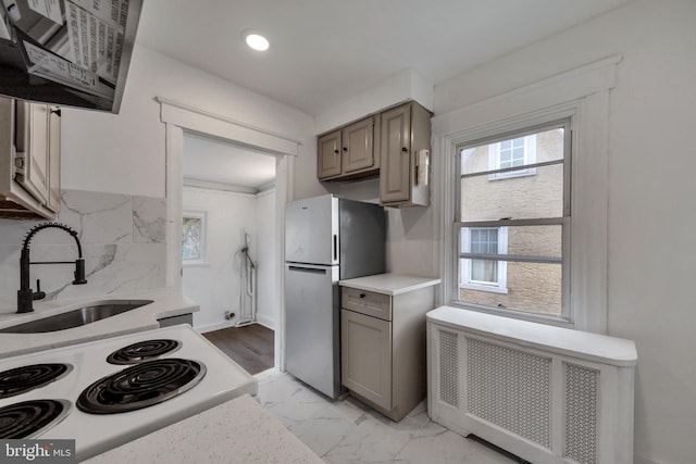 kitchen featuring exhaust hood, white range, sink, radiator heating unit, and stainless steel refrigerator