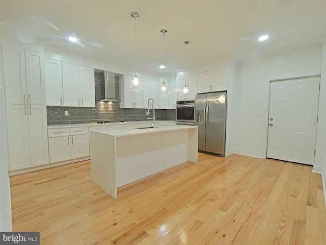 kitchen with white cabinetry, appliances with stainless steel finishes, wall chimney range hood, and decorative light fixtures